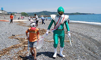 緑色の明社レンジャーと少年が砂浜でゴミ拾い